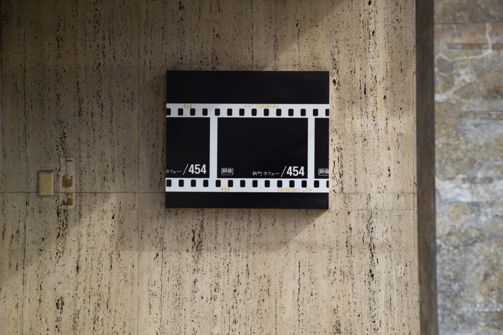 鞆町カフェー454の外壁に設置された、フィルムデザインの黒い看板の写真
